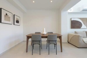 A modern dining area with a wooden table, four grey chairs, and a white pitcher. - Athenean Pool Heaven (ELLINIKO)