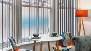 Een eetruimte met een tafel, stoelen en uitzicht op een gebouw door een raam.