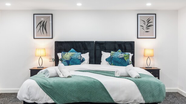 Een hotelkamer met een bed, twee nachtkastjes, twee wandlampen en twee kunstwerken in lijst.