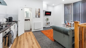 Een moderne keuken met een koffieapparaat, een wasmachine en een eethoek met een grijze bank en oranje vloerkleed.
