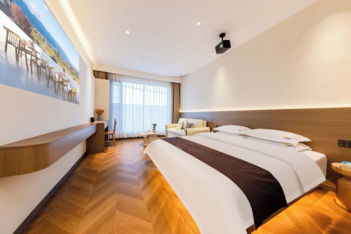 Une chambre d’hôtel avec un grand lit, un bureau, une chaise, un canapé et une grande fenêtre.