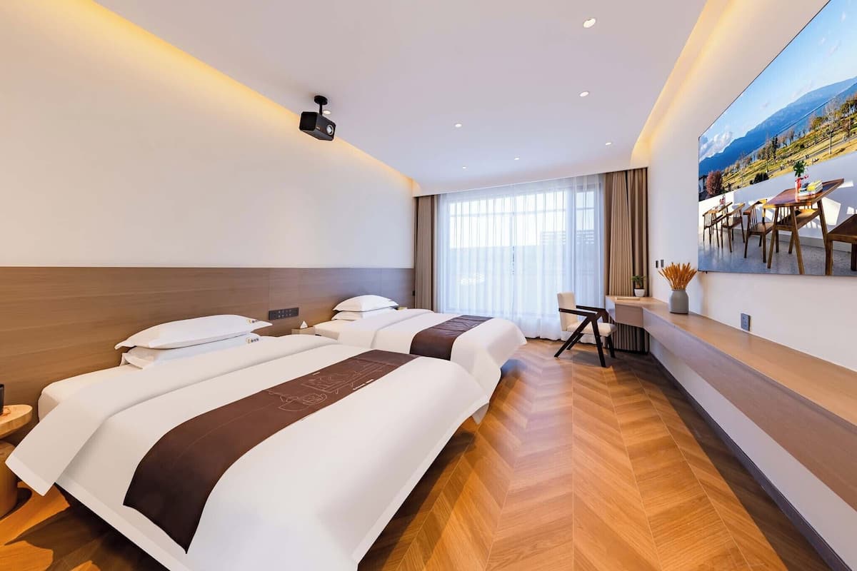 Une chambre d’hôtel avec deux lits, un bureau et une grande fenêtre donnant sur la montagne.