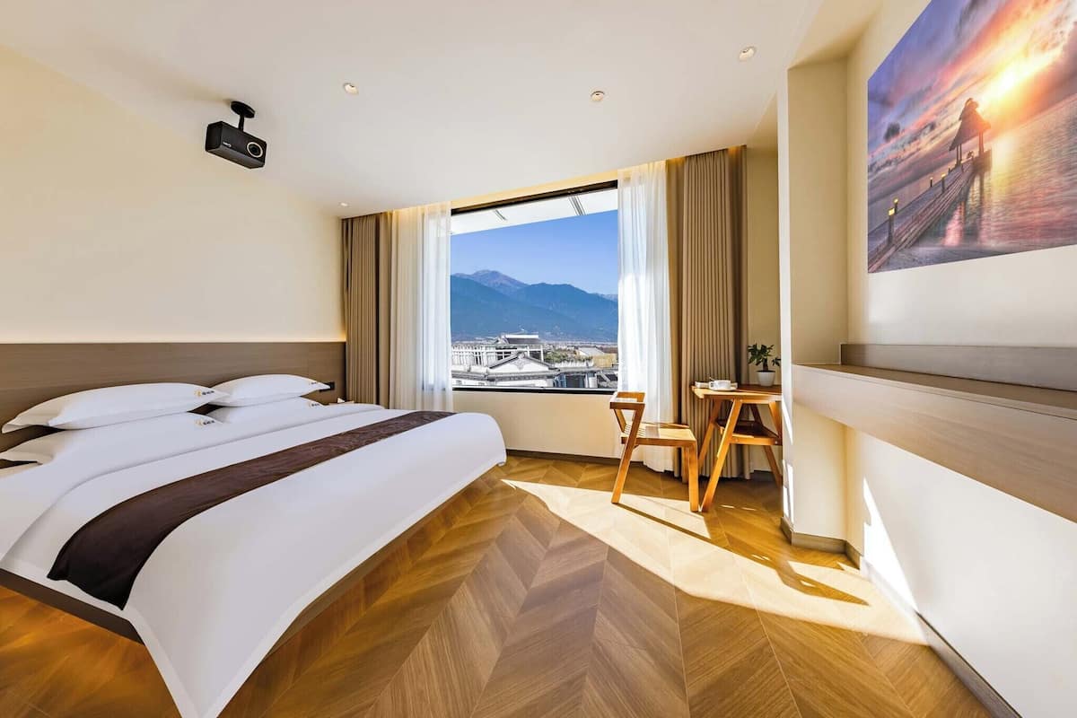 Une chambre d’hôtel avec un grand lit, un bureau, une chaise, un projecteur et un tableau.