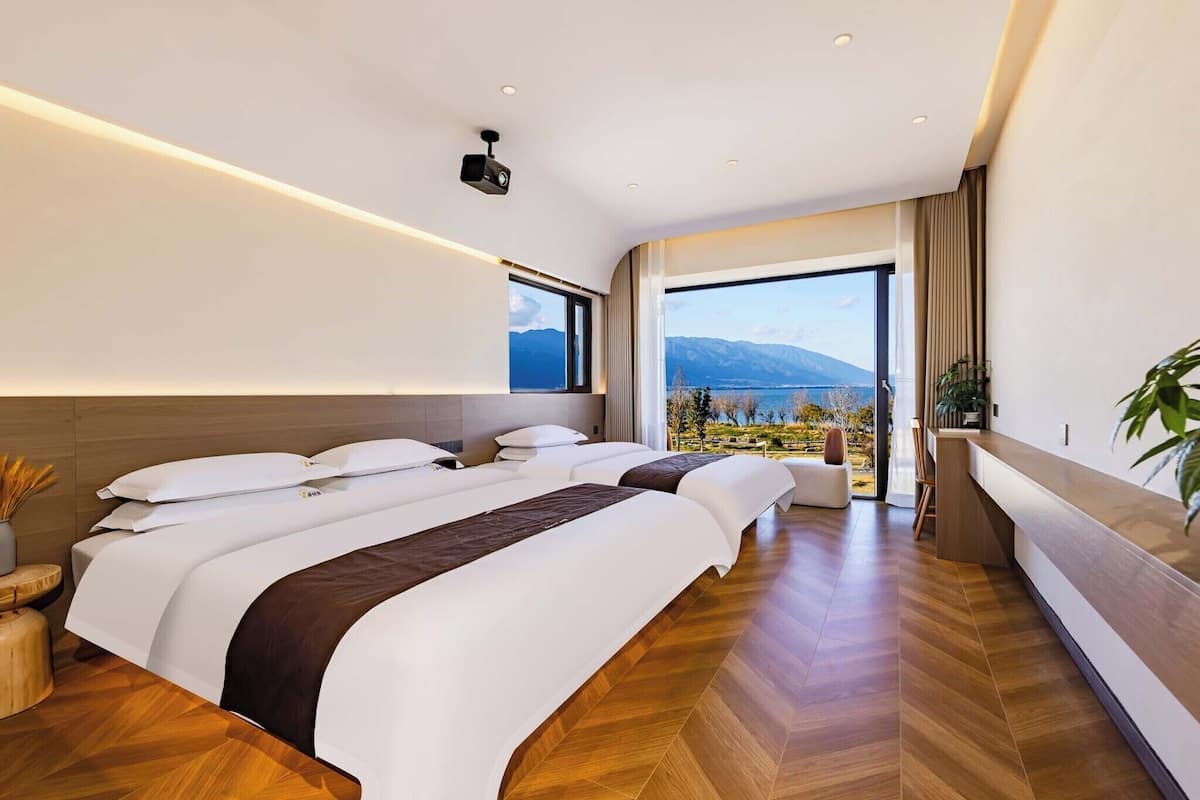 Une chambre d’hôtel avec trois lits, une grande fenêtre donnant sur les montagnes, un plancher en bois et un design moderne.