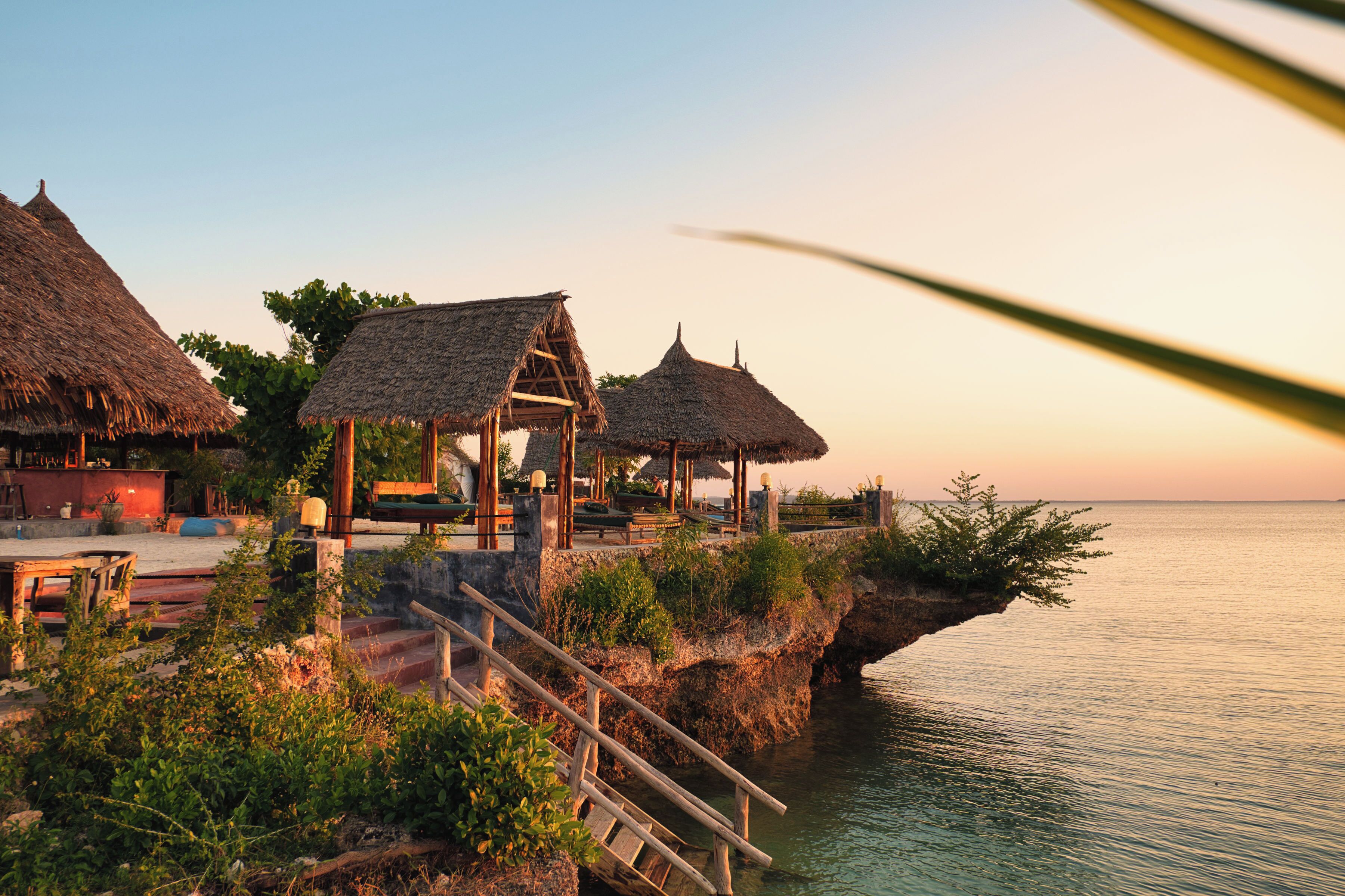 A coastal resort with thatched-roof structures, a wooden staircase, and a view of the sea.