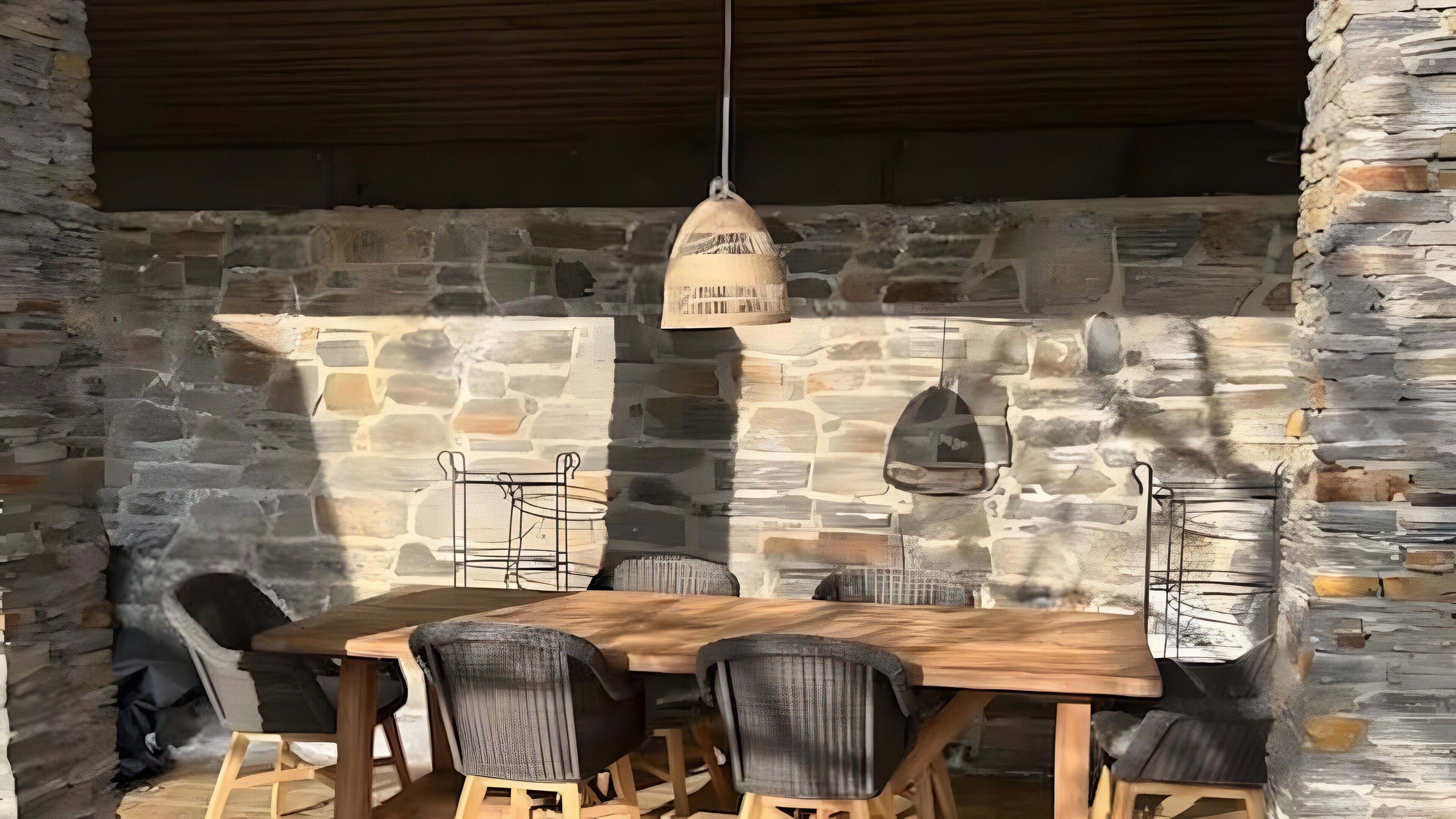Un espace extérieur aménagé pour les repas, avec des murs en pierre, une table et des chaises en bois, un luminaire suspendu et un banc en pierre.