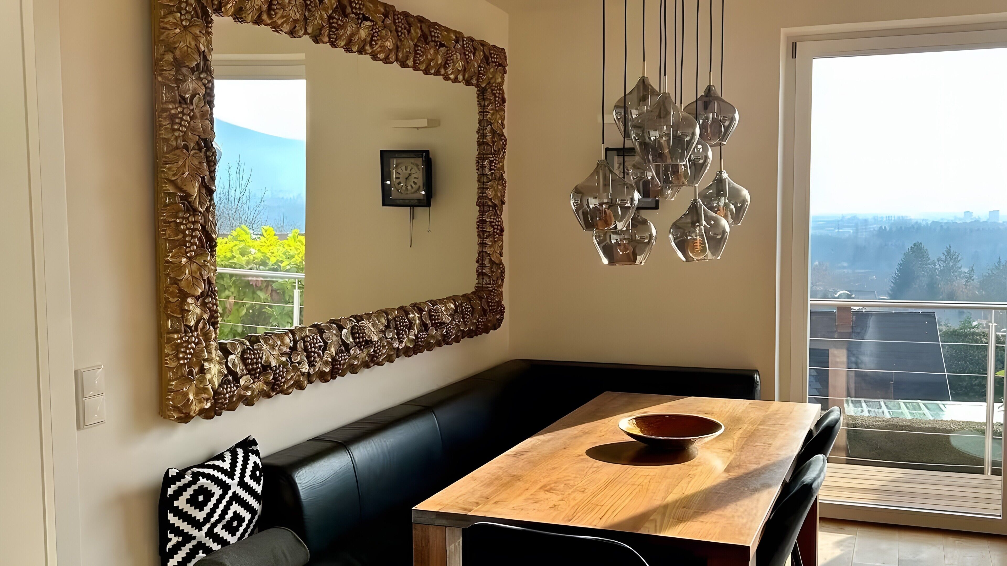 Un comedor con una mesa de madera, un banco de cuero negro y un espejo decorativo con motivos florales.