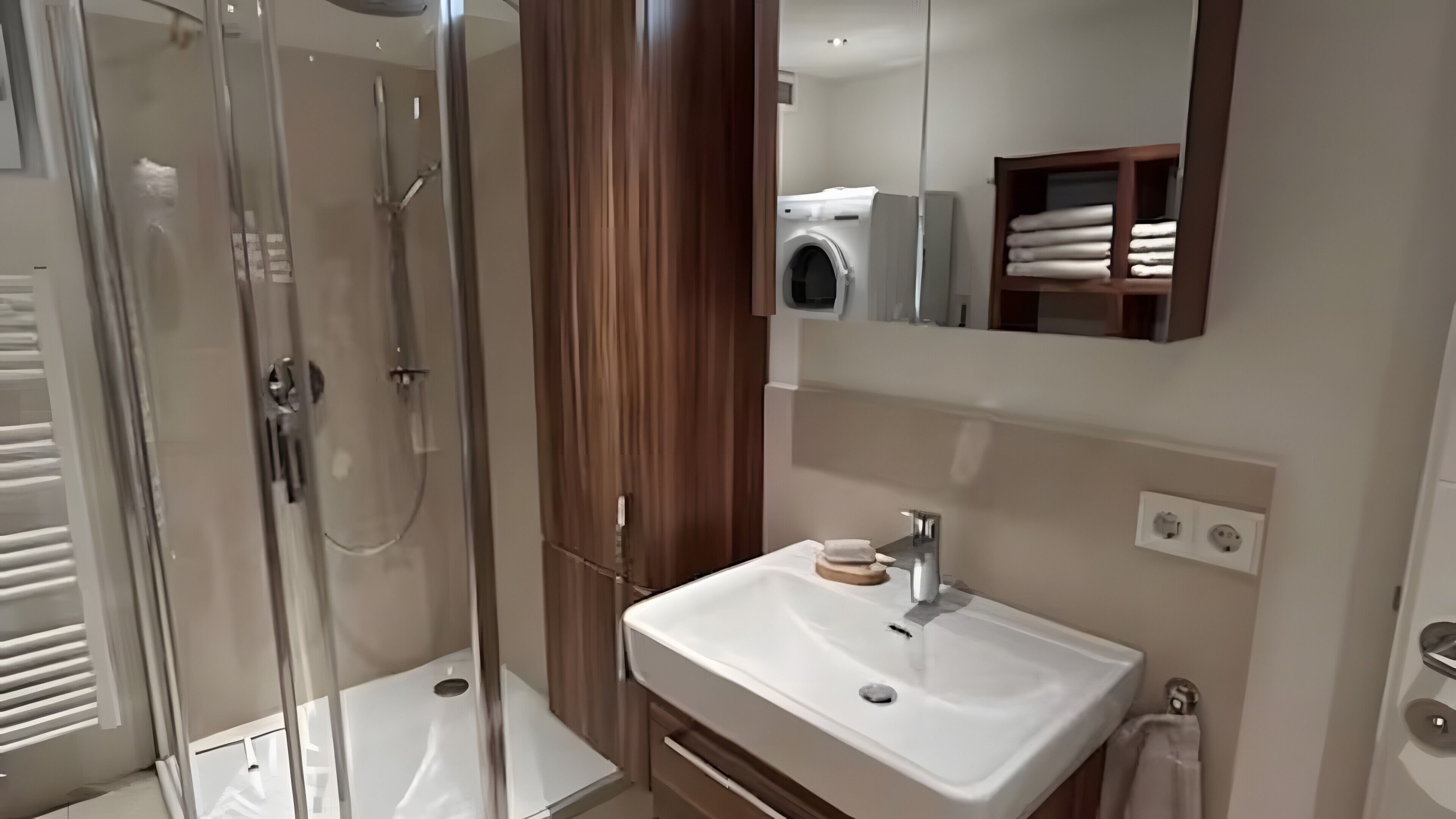 Ein Badezimmer mit einer ein Glasfachwerk-eingefassten Dusche, einem weißen Waschbecken und einem Spiegel darüber.