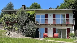 A two-story building with a balcony, a stone staircase, and a garden area.