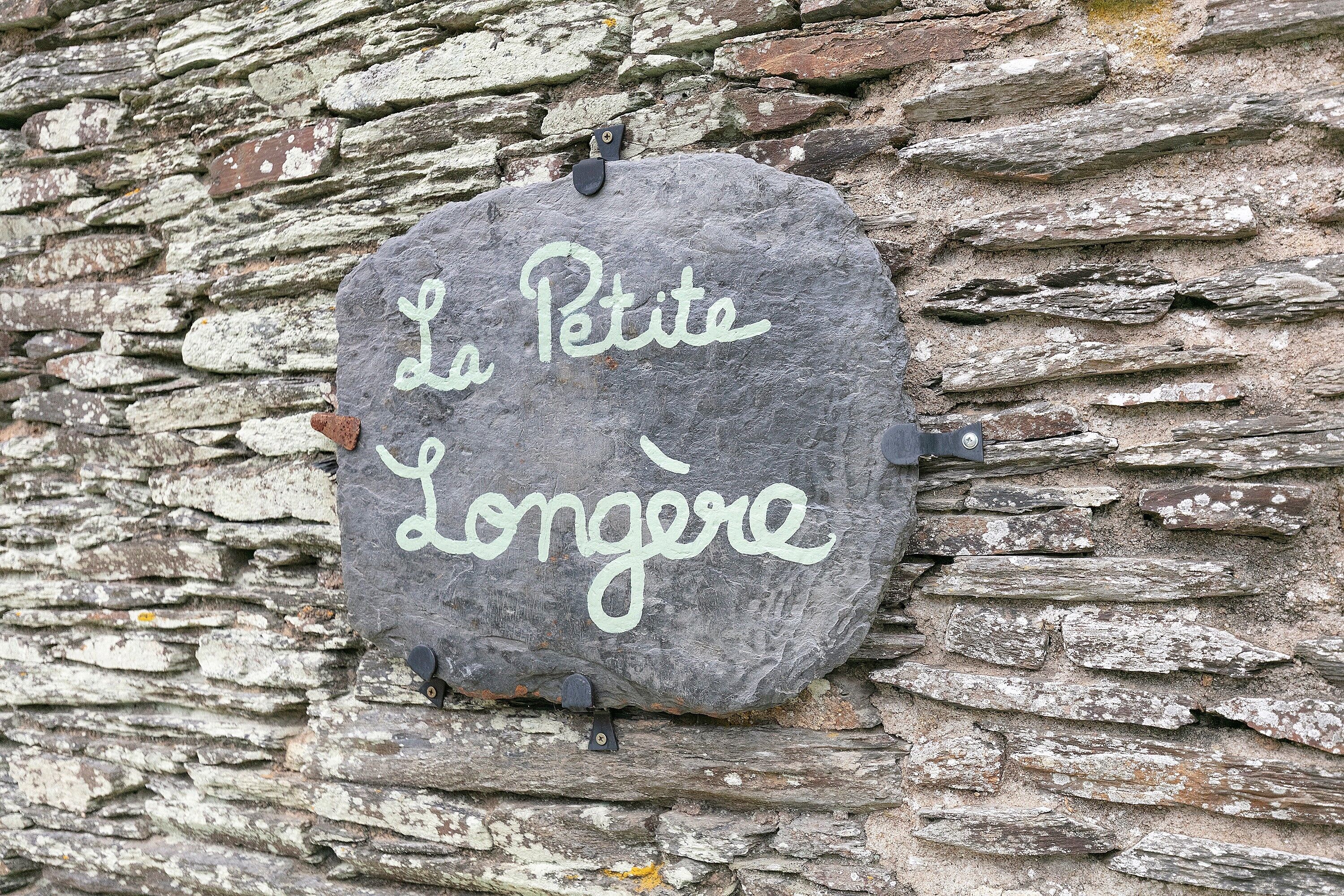 A stone sign with the inscription 'La Petite Longère' mounted on a stone wall.