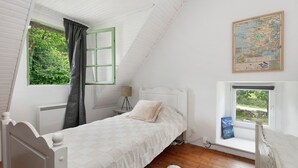 A bedroom with a single bed, a window with a view of greenery, a map on the wall, and a small table with a lamp. - Gîte La P'tite Longère – Independent Cottage in a Peaceful Countryside Setting (Saint-Jacut-les-Pins)