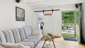 A living room with a striped sofa, a glass table with a vase, and a door leading to an outdoor area with a table and chairs. - Gîte La P'tite Longère – Independent Cottage in a Peaceful Countryside Setting (Saint-Jacut-les-Pins)