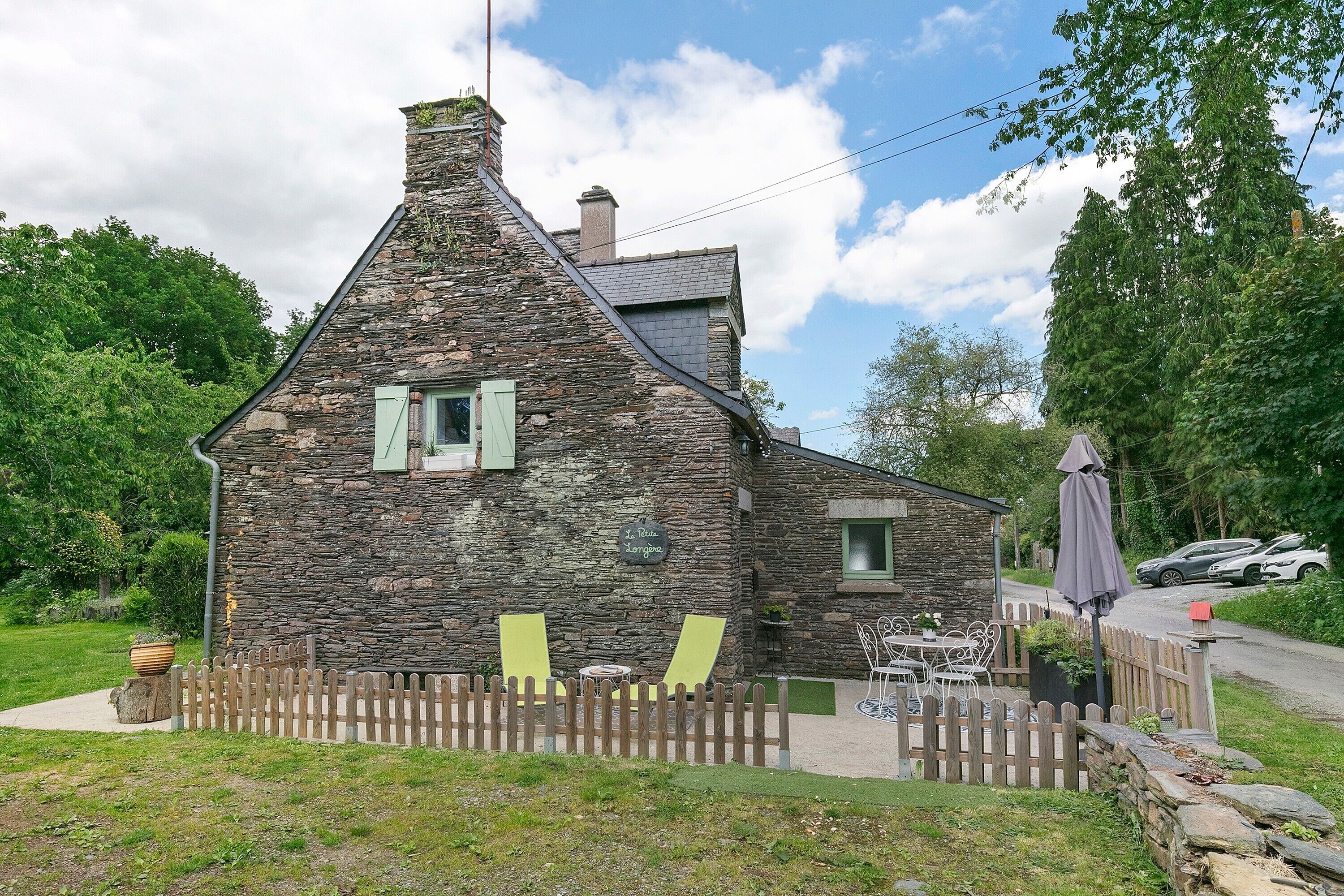 A stone house with a sloped roof, a wooden fence, and outdoor seating.