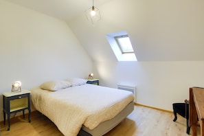 Une chambre à coucher avec un lit, une table de chevet avec une lampe, une chaise en bois, un puits de lumière et un luminaire suspendu.