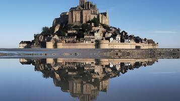 A historic castle-like structure with a prominent tower, situated on a rocky island with calm water reflecting its image.