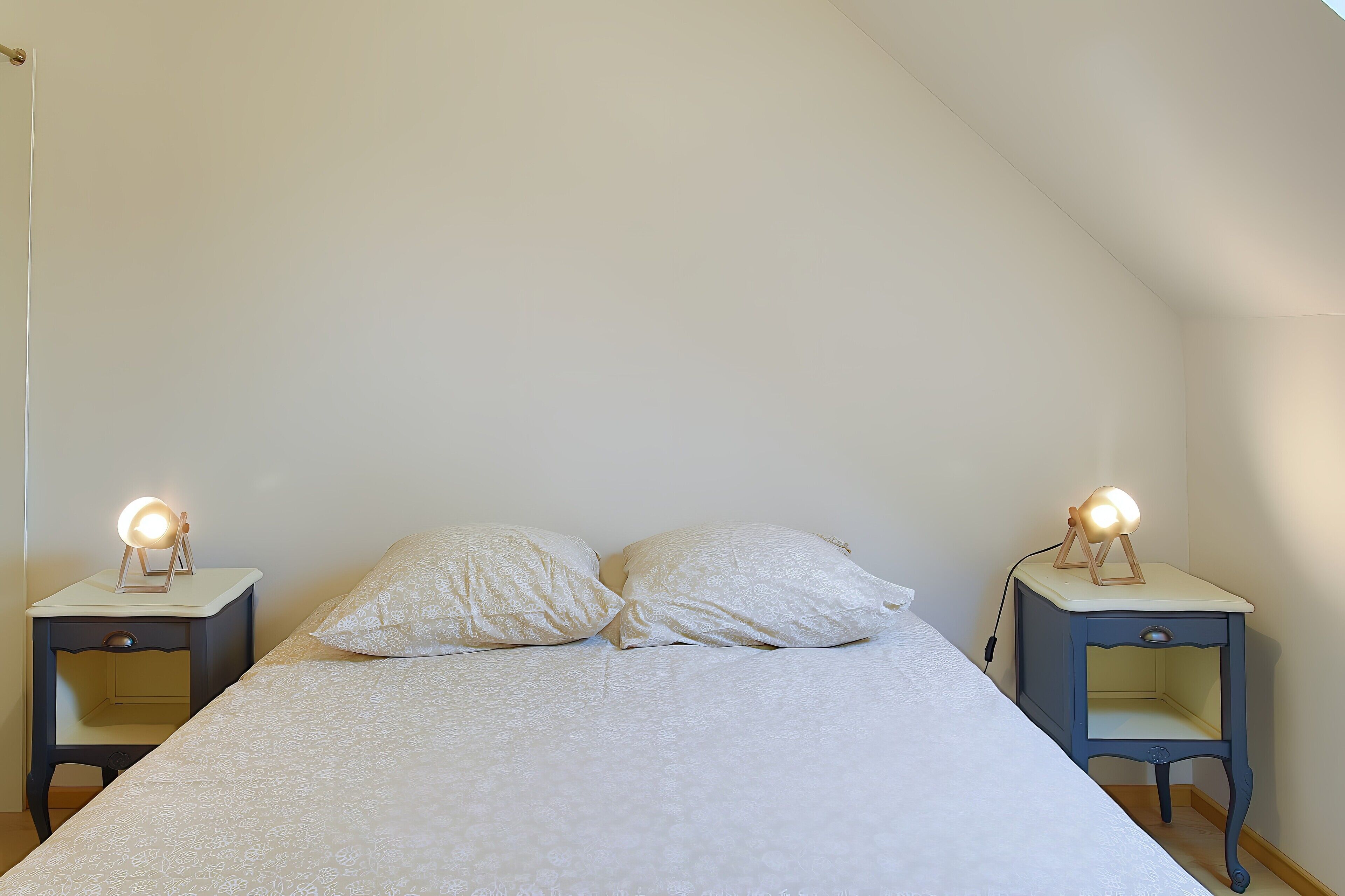 Une chambre à coucher avec un lit, deux tables de chevet et deux lampes.