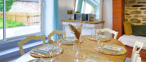 Una mesa de comedor con manteles individuales, cristalería y cubiertos, con una pared de piedra y un banco de madera al fondo.