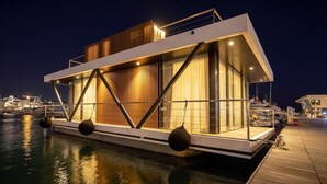A modern floating structure with a deck, large windows, and a wooden facade. - Marina Suite (Loano)