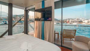 A modern hotel room with a large bed, a TV, a balcony with a view of the marina, and a wooden table. - Marina Suite (Loano)
