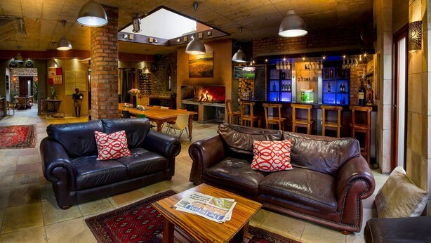 A cozy lounge area with leather sofas, a fireplace, and a bar with bottles. - Madiba Bay Guesthouse (Gqeberha)
