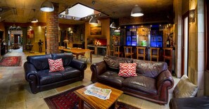 A cozy lounge area with leather sofas, a fireplace, and a bar with bottles. - Madiba Bay Guesthouse (Gqeberha)