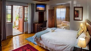 A bedroom with a bed, desk, chair, TV, and a view of the outdoors. - Madiba Bay Guesthouse (Gqeberha)