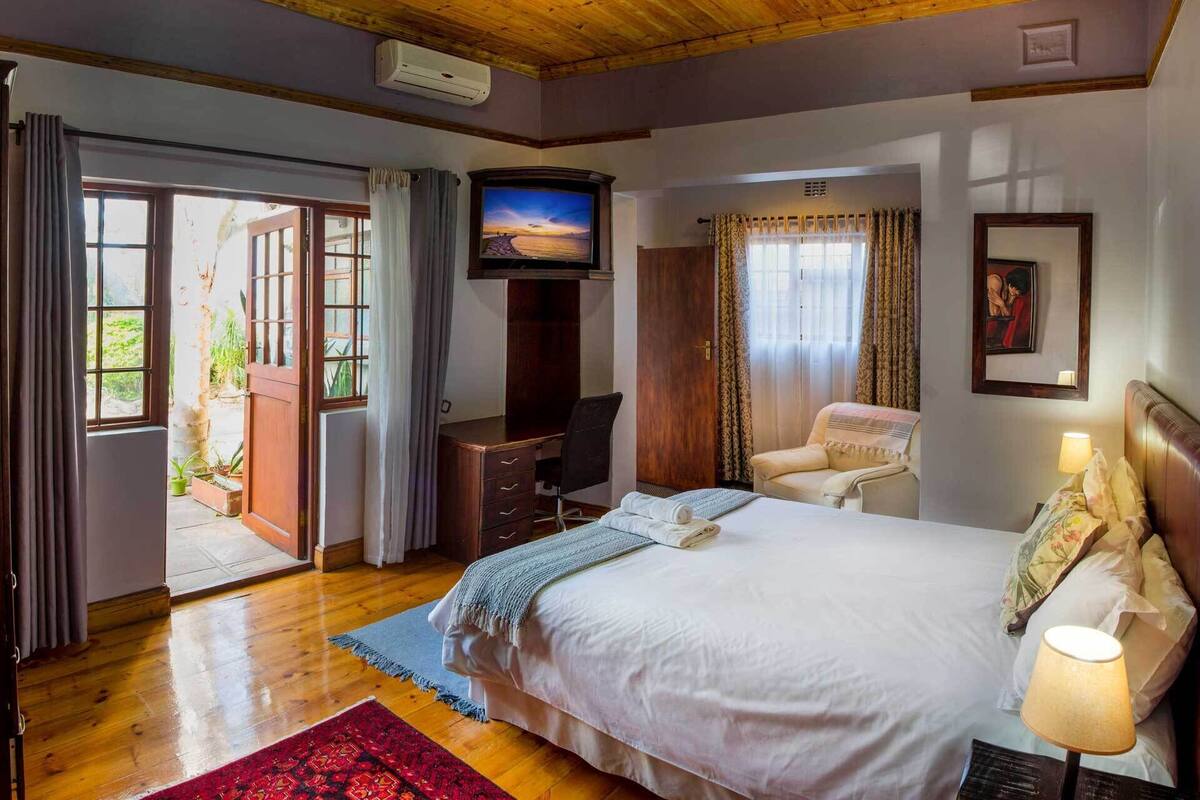 A bedroom with a bed, desk, chair, TV, and a view of the outdoors.