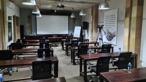 A conference room with multiple tables and chairs, a projector screen, and a large poster on the wall. - Madiba Bay Guesthouse (Gqeberha)