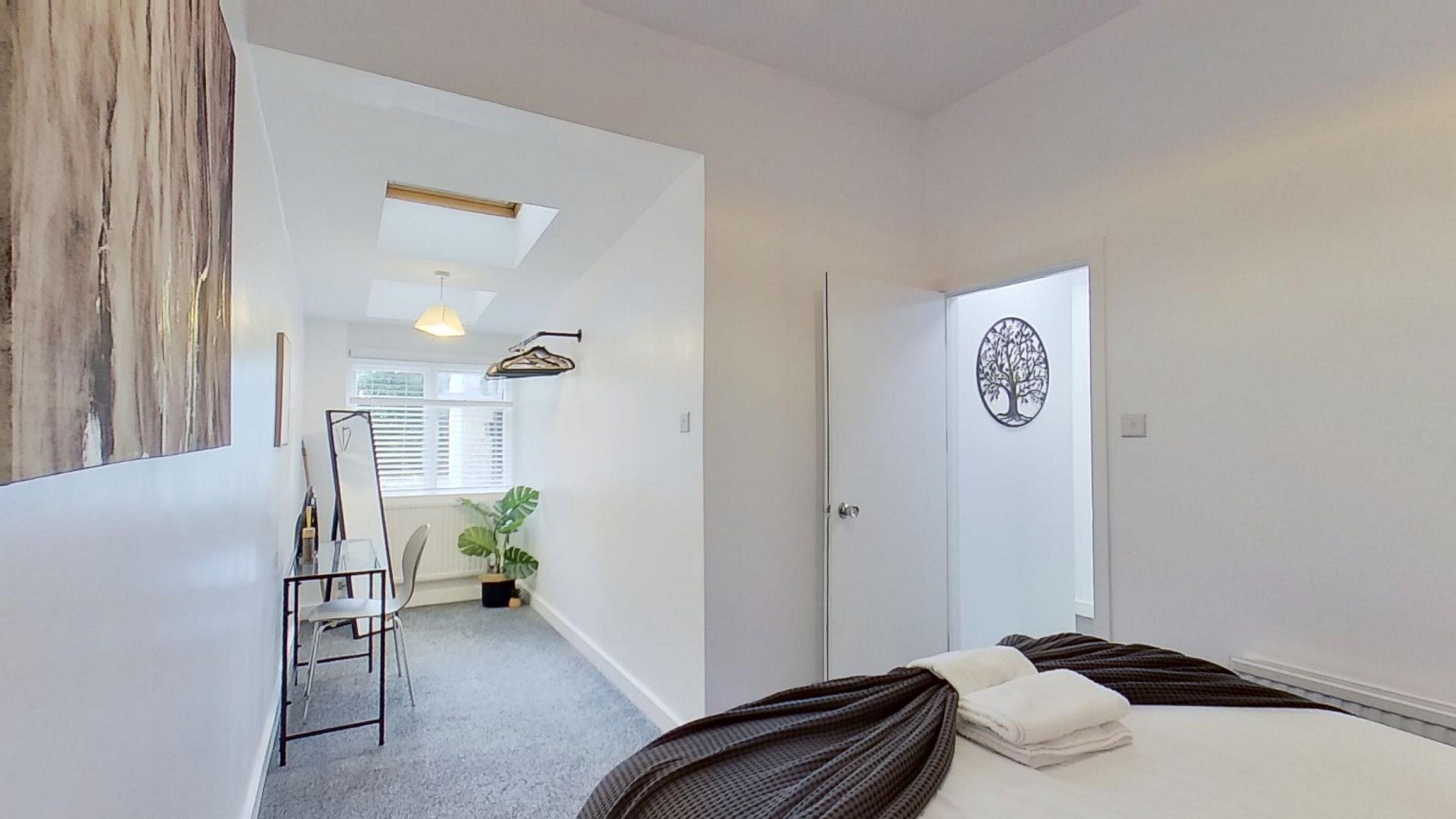 A bedroom with a bed, a door with a tree decal, a chair, a plant, and a skylight.
