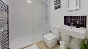 A modern bathroom with a glass-enclosed shower, a white toilet, a sink with a black-tiled backsplash, and a framed picture on the wall. - Charming 2 Bed Apt with Netflix & Wi-Fi (London)