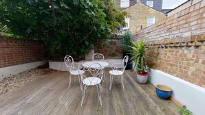 A patio with a table and chairs, surrounded by a brick wall and greenery. - Charming 2 Bed Apt with Netflix & Wi-Fi (London)