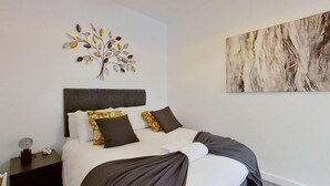 A neatly made bed with a headboard, a wall art piece above it, and a painting on the adjacent wall. - Charming 2 Bed Apt with Netflix & Wi-Fi (London)
