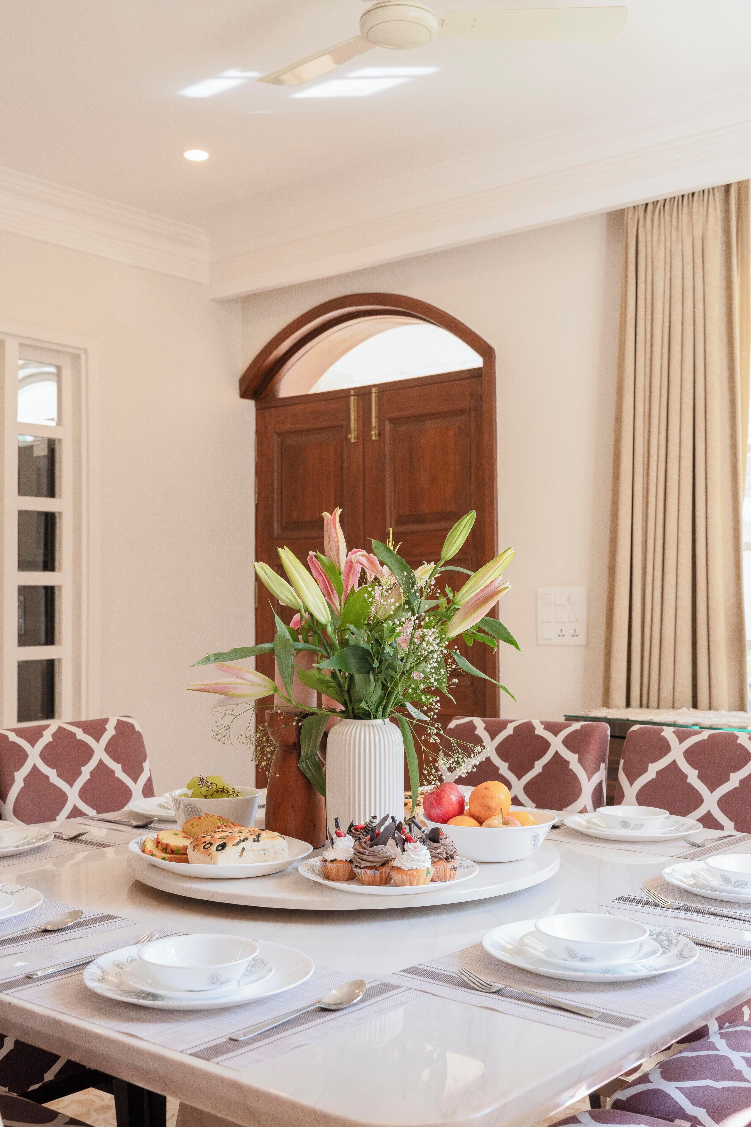 A dining area with a table set for a meal, a vase of flowers, and a wooden door in the background.