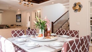 A dining area with a long table set for six, surrounded by patterned chairs, a vase of flowers, and a decorative wall clock. - Staymaster Terra Tango 4BR Villa (Calangute)