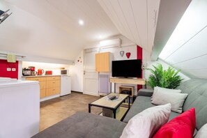 Een ruimtelijk ingerichte leefruimte met een kitchenette, een bank, een televisie en een kleine tafel.