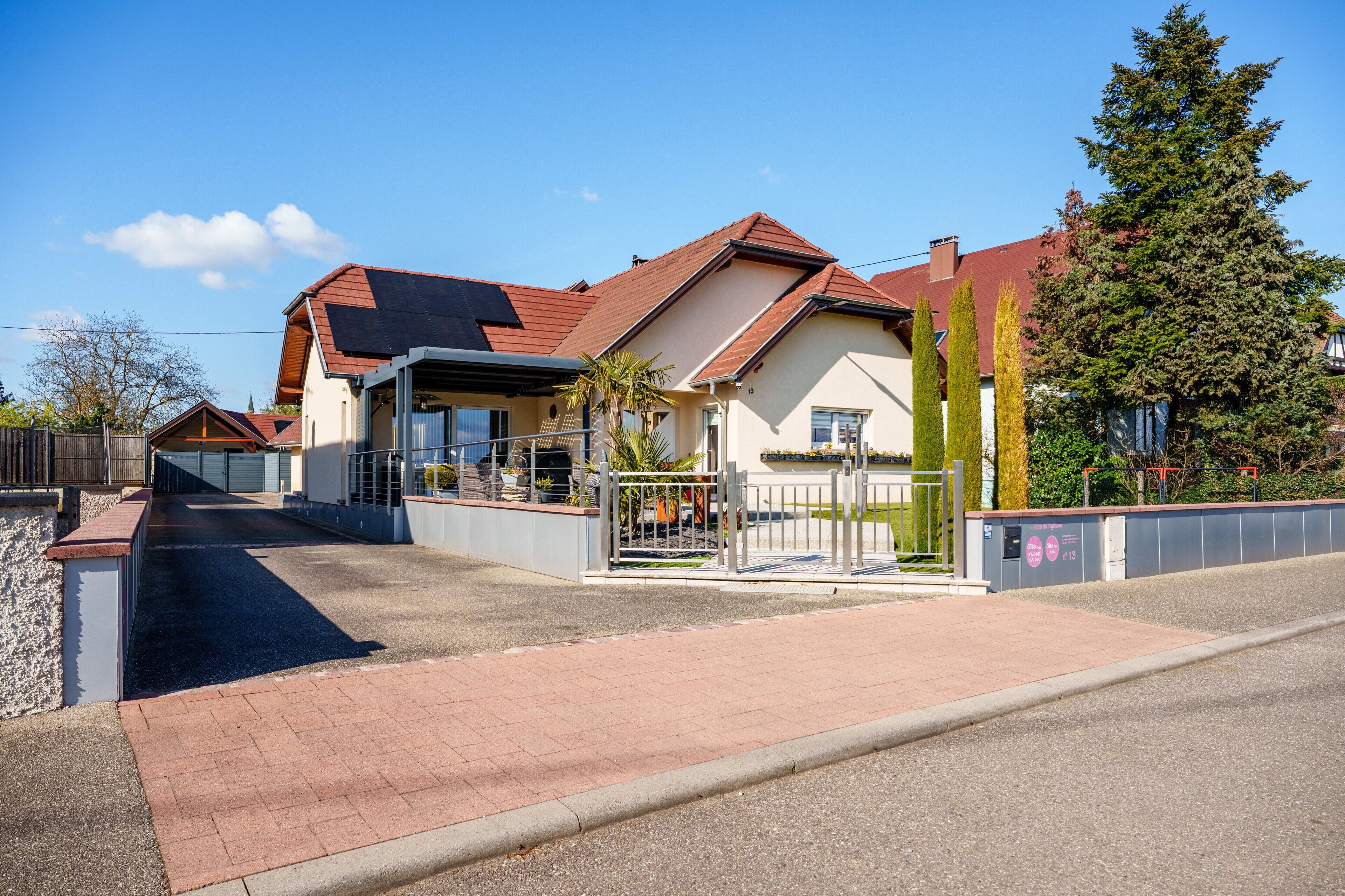 A residential house with a paved driveway, a gated entrance, and a solar panel on the roof.