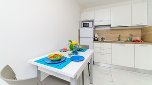 A compact kitchen with white cabinets, a microwave, a sink, and a dining table set with plates, a bowl of fruit, and a vase. - Lily Suite (Massa Lubrense)