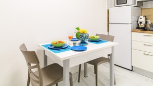 A white dining table with blue placemats, two chairs, a vase with lemons, and bowls with food. - Lily Suite (Massa Lubrense)
