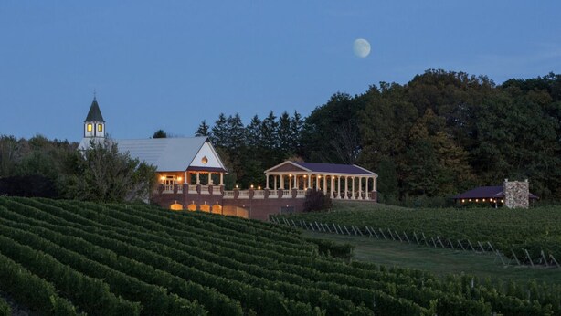 A vineyard with rows of grapevines, a large building with a triangular roof, and a tower in the background. - This is ideal for families, SPIRE & winery visits. (Geneva-on-the-Lake)