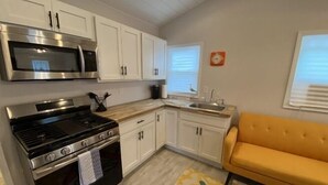 A compact kitchen with white cabinets, a stainless steel microwave, a gas stove, and a yellow sofa. - This is ideal for families, SPIRE & winery visits. (Geneva-on-the-Lake)