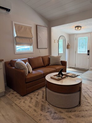 A living room with a brown leather sofa, a round coffee table, and a patterned rug. - Dog-friendly 2BR with fireplace, 7 miles to SPIRE and minutes from the wineries. (Geneva-on-the-Lake)