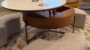 A round wooden table with a white top, surrounded by four ottomans, in a living room with a sofa and a window. - This is ideal for families, SPIRE & winery visits. (Geneva-on-the-Lake)