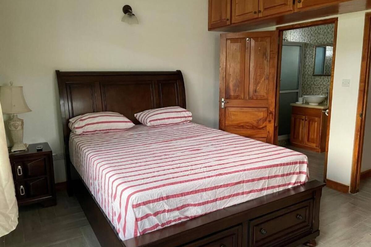 A bedroom with a wooden bed, a nightstand, a wardrobe, and a bathroom visible through an open door.