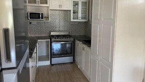 A compact kitchen with white cabinets, a microwave, a stove, and a tiled backsplash. - Travellers Villa (Roseau)