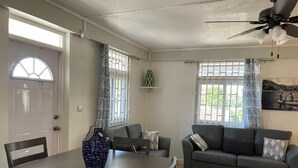 A living room with a dining table, two sofas, a ceiling fan, and a window with patterned curtains. - Travellers Villa (Roseau)