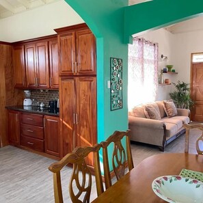 A kitchen with wooden cabinets, a dining table with chairs, a sofa, and a decorative wall piece. - Travellers Villa (Roseau)