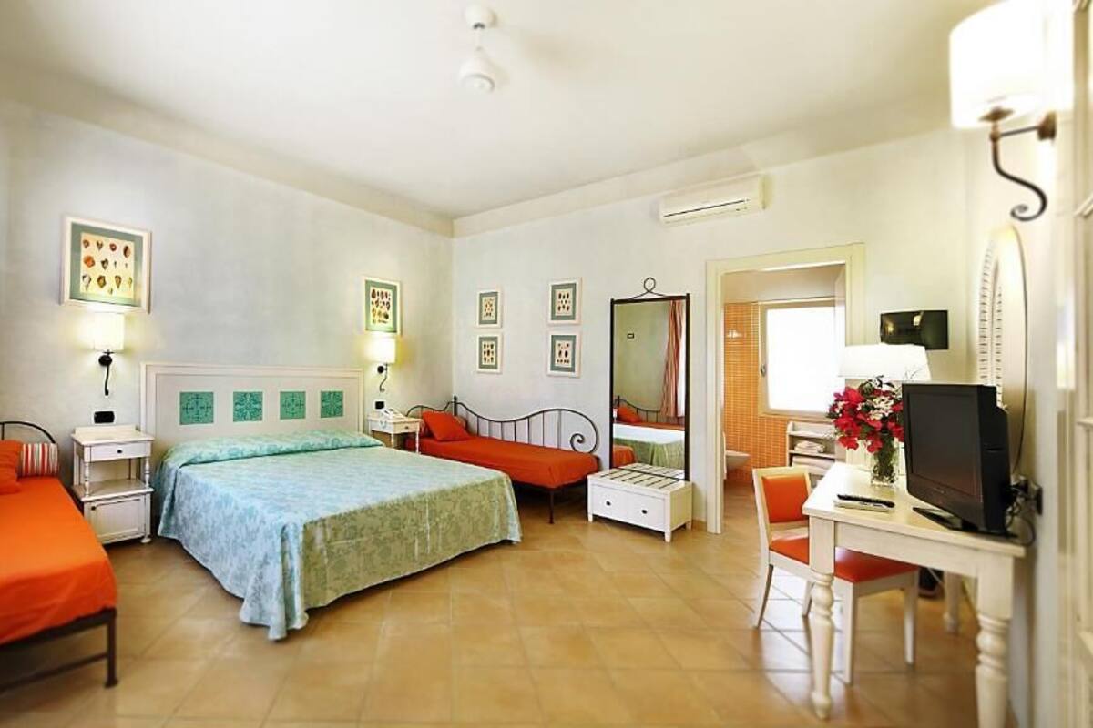 A bedroom with two beds, a desk, a chair, a TV, and a mirror.