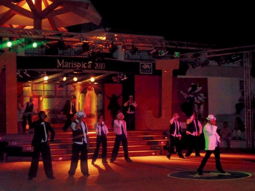 A stage with performers in black and white outfits, a sign reading 'Marispica 2010', and a logo for 'IGV CLUB'.