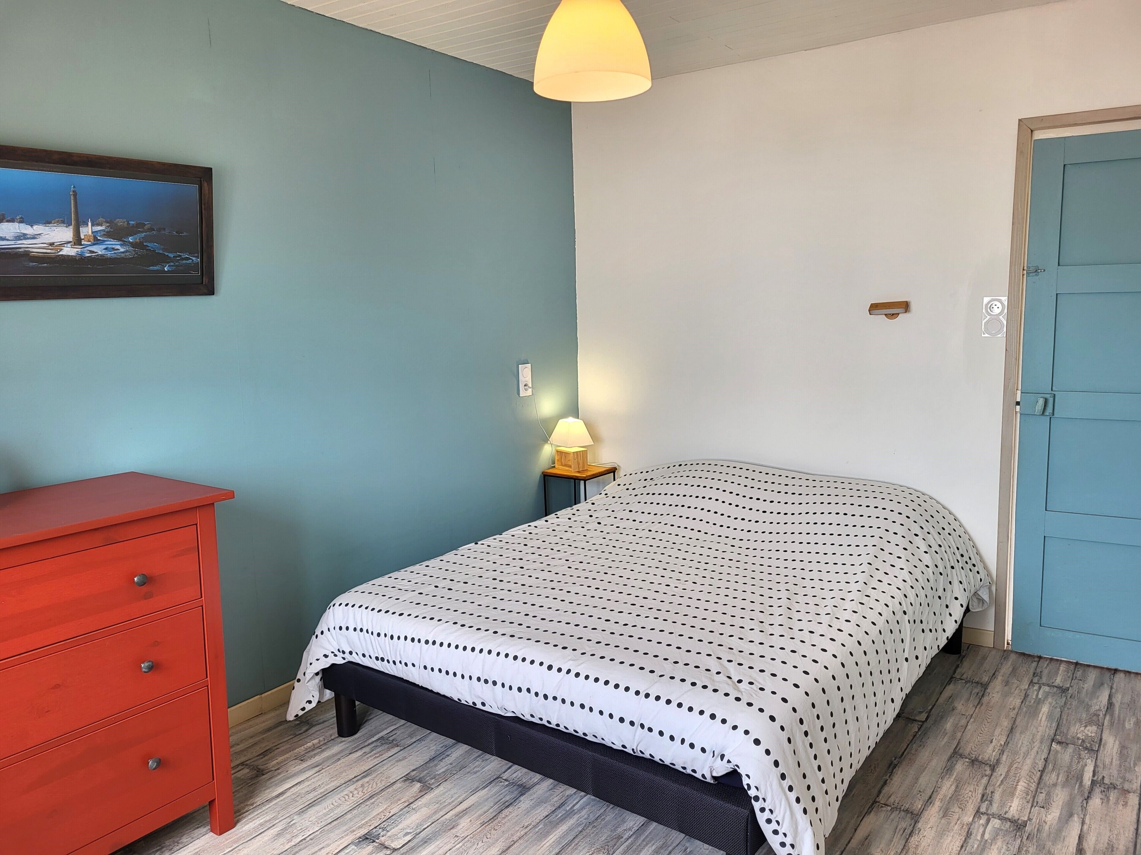 A bedroom with a bed, a red dresser, a lamp, and a door.