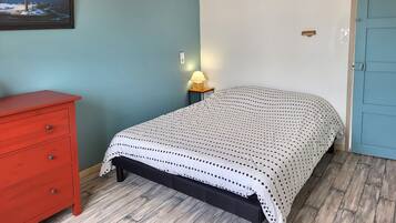 A bedroom with a bed, a red dresser, a lamp, and a door.